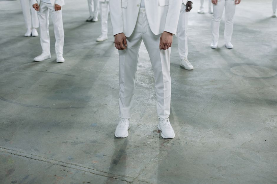 A pair of pristine white leather sneakers styled with grey tailored trousers and a light blue shirt, suitable for a business casual environment.