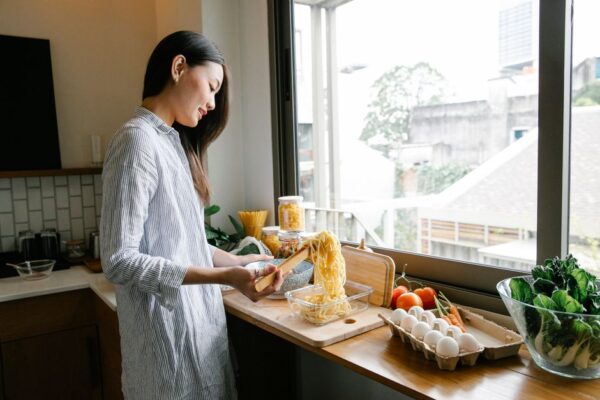 A woman smiling while quickly assembling ingredients for dinner in a clean, modern kitchen.