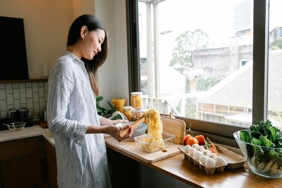 A woman smiling while quickly assembling ingredients for dinner in a clean, modern kitchen.