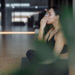 A woman with headphones in, sitting calmly in an airport lounge, practicing deep breathing exercises with her eyes closed.