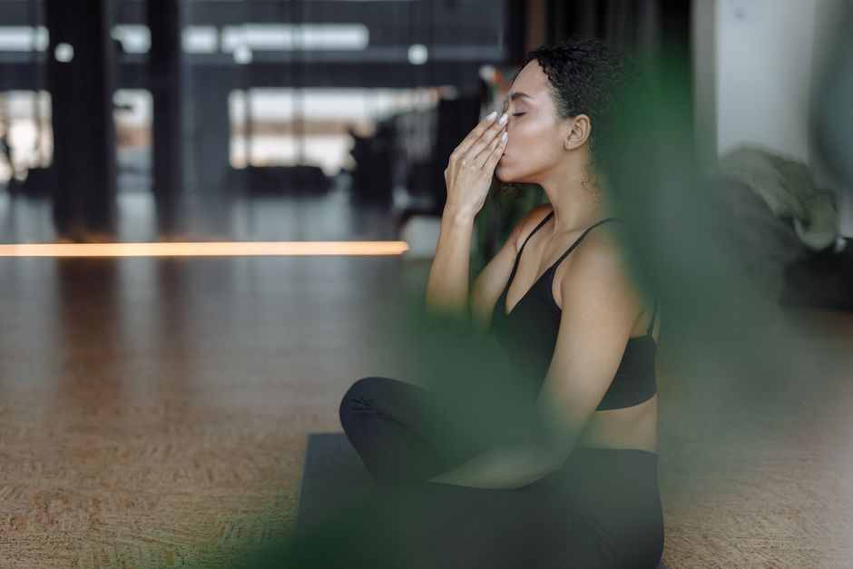 A woman with headphones in, sitting calmly in an airport lounge, practicing deep breathing exercises with her eyes closed.
