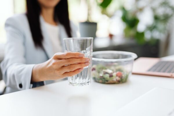 A busy woman in a modern office setting eating a healthy, balanced lunch from a bento box, looking focused and energized.