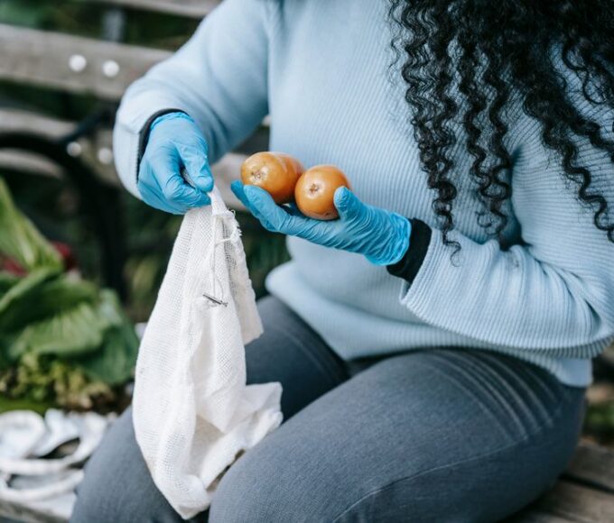 A busy woman smiling, holding a reusable canvas bag full of fresh produce, shopping at an outdoor farmers market.