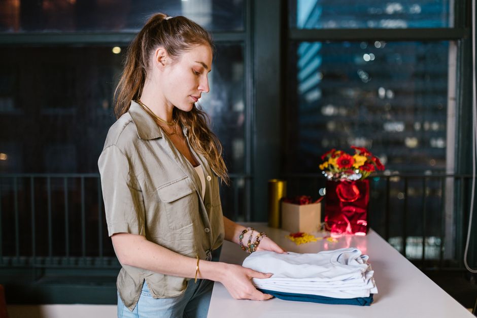 A person efficiently folding clean t-shirts on a small kitchen counter in a modern, tidy apartment, demonstrating organized laundry habits.