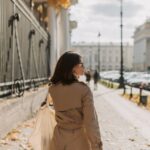 A professional woman in a classic beige trench coat walking purposefully on a rainy city street with an umbrella.