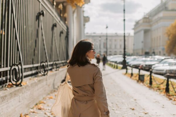 A professional woman in a classic beige trench coat walking purposefully on a rainy city street with an umbrella.