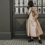 A stylish woman in London wearing a cream knit sweater, tailored camel trousers, and a dark long coat, demonstrating texture and neutral layering.