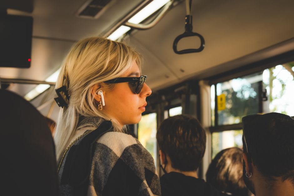 A woman smiling slightly while listening to a podcast on a bus, with city lights blurred in the background, showing commute relaxation.