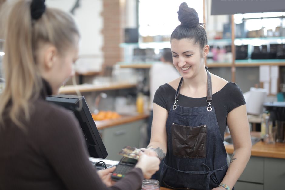 A woman using a credit card to pay for coffee and pastries at an outdoor cafe in a European city.