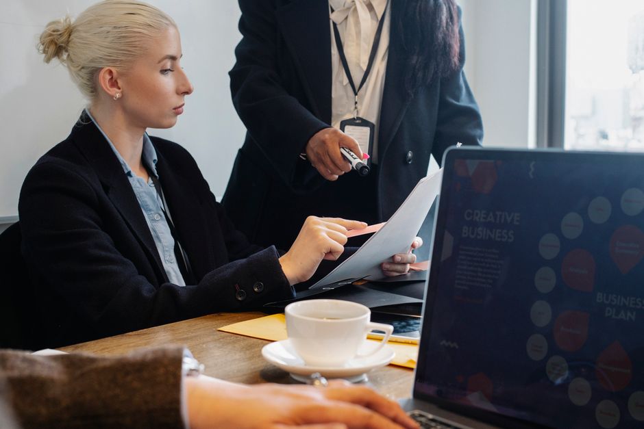 A professional woman in an office setting, actively working on a laptop with presentation slides visible, possibly brainstorming with an AI tool.