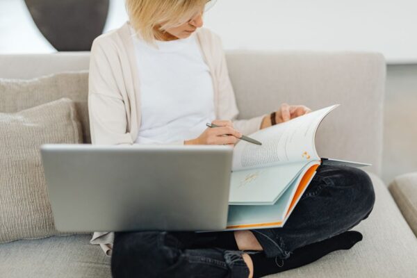 A remote worker taking a break to read a book on a comfortable sofa, laptop nearby, demonstrating how to fit reading into a busy schedule.