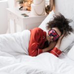 A woman with noise-canceling headphones and an eye mask sleeping peacefully in an airplane window seat during a red-eye flight.