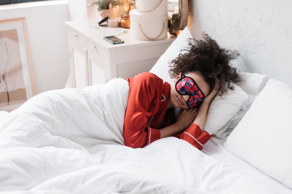 A woman with noise-canceling headphones and an eye mask sleeping peacefully in an airplane window seat during a red-eye flight.