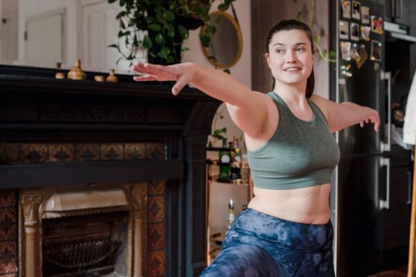 A woman in athletic wear performing a gentle stretch on a yoga mat in her bright living room, symbolizing home fitness.