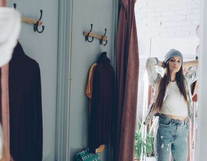 A woman in a brightly lit denim store trying on a pair of well-fitting straight-leg jeans, looking in a mirror.