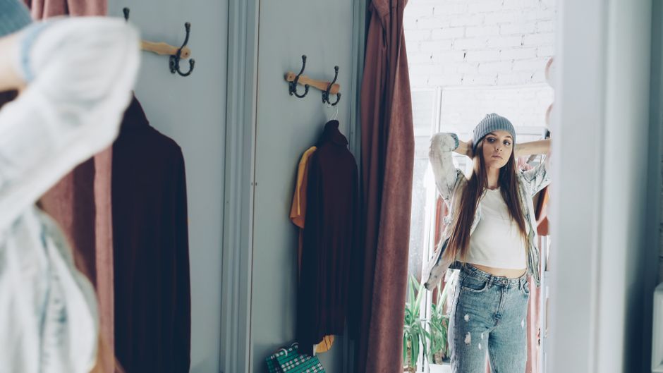 A woman in a brightly lit denim store trying on a pair of well-fitting straight-leg jeans, looking in a mirror.