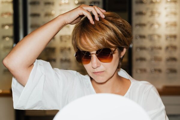 A woman trying on different pairs of sunglasses in a modern eyewear store, looking into a mirror.