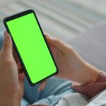 A woman smiling, looking at her phone displaying an AI styling app with various outfit combinations suggested by virtual stylist technology.