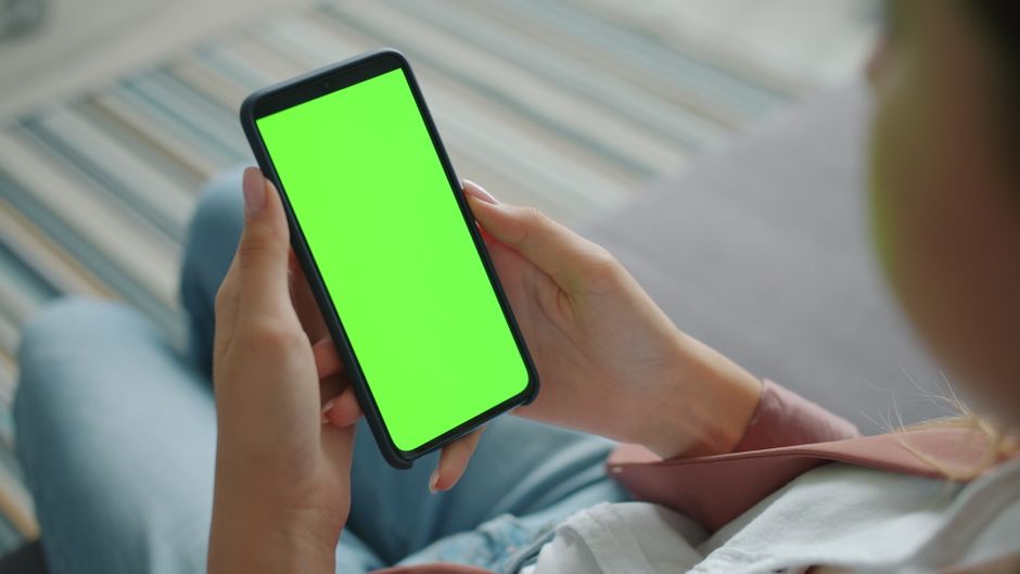 A woman smiling, looking at her phone displaying an AI styling app with various outfit combinations suggested by virtual stylist technology.