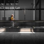 Woman in comfortable layers walking through a modern, brightly lit airport terminal, carrying a small travel bag and looking relaxed.