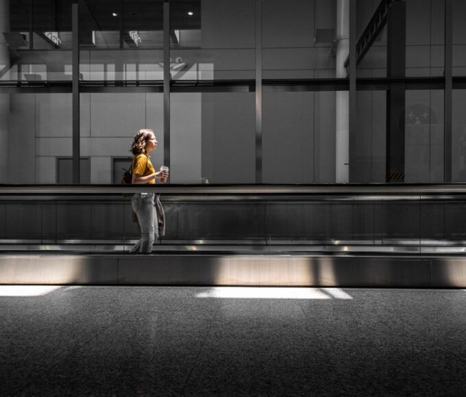 Woman in comfortable layers walking through a modern, brightly lit airport terminal, carrying a small travel bag and looking relaxed.