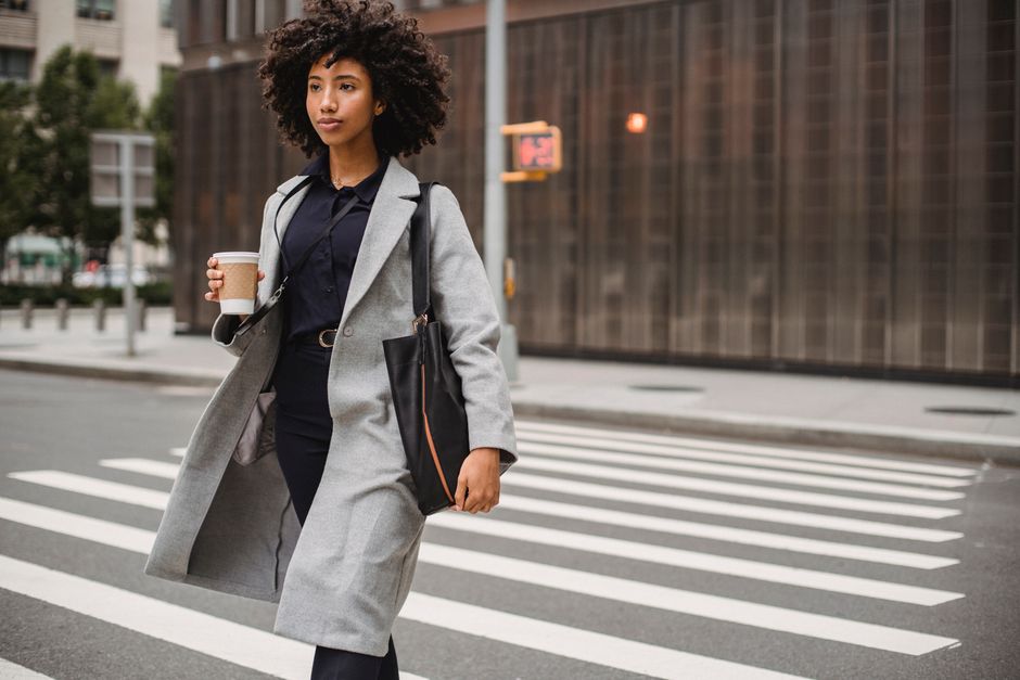 A young professional woman in a light, flowing summer work outfit walks confidently down a sunny city street, showcasing a comfortable yet chic summer work wardrobe for hot cities.