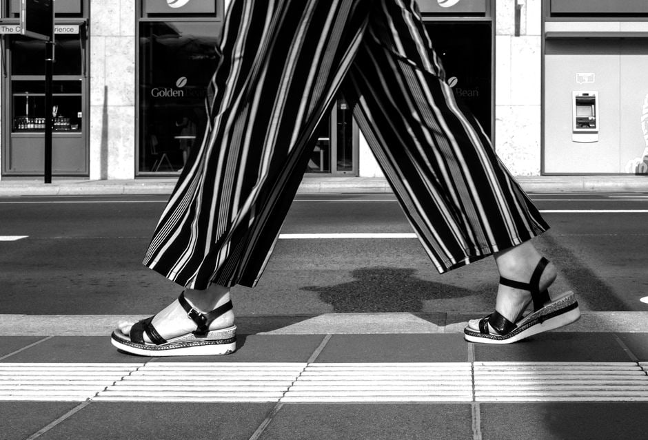 A woman wearing stylish black wide-leg pants, a fitted top, and a blazer, walking confidently in a modern city setting.