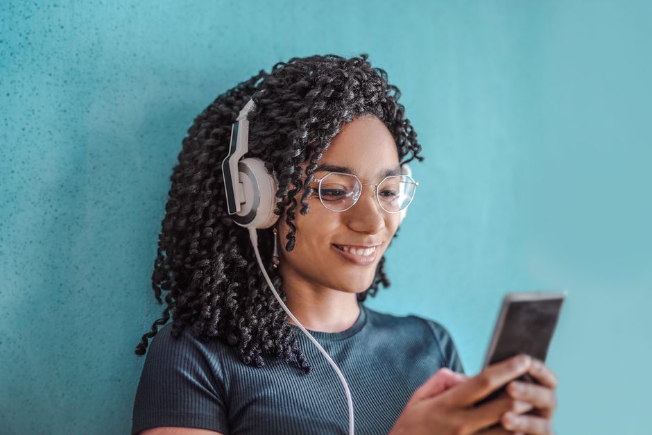 A focused woman wearing headphones, actively speaking into a smartphone while an AI language learning app displays real-time pronunciation analysis and grammatical corrections.