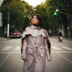 A stylish woman in a beige trench coat walks confidently down a bustling city street on a mild spring day.