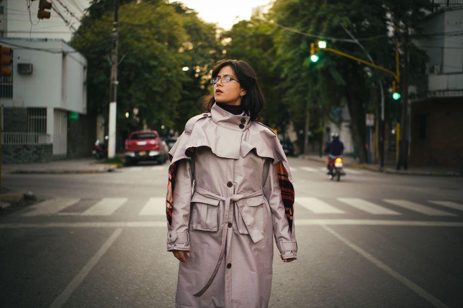 A stylish woman in a beige trench coat walks confidently down a bustling city street on a mild spring day.