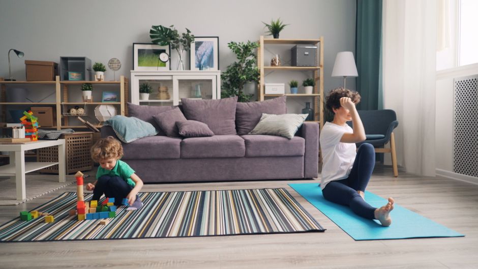 A neatly rolled yoga mat placed on a wooden floor in a cozy, bright apartment living room, ready for a workout.