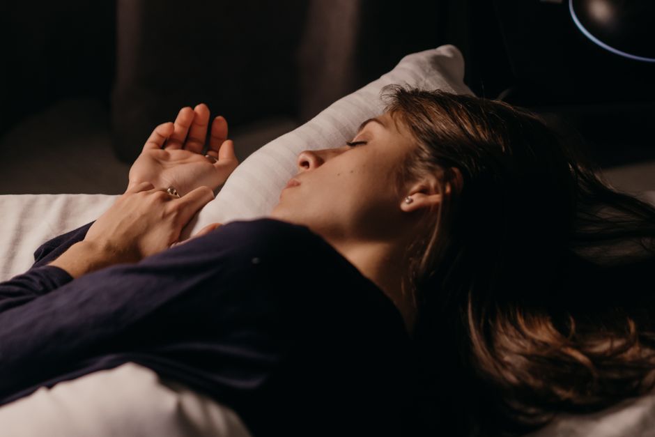 A serene bedroom at night with thick blackout curtains drawn, a small white noise machine on a bedside table, and only minimal light from a digital clock, symbolizing an optimized sleep environment.