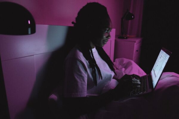 A person in a city apartment working on a laptop late at night, surrounded by dimly lit skyscrapers outside the window, illustrating late work hours.